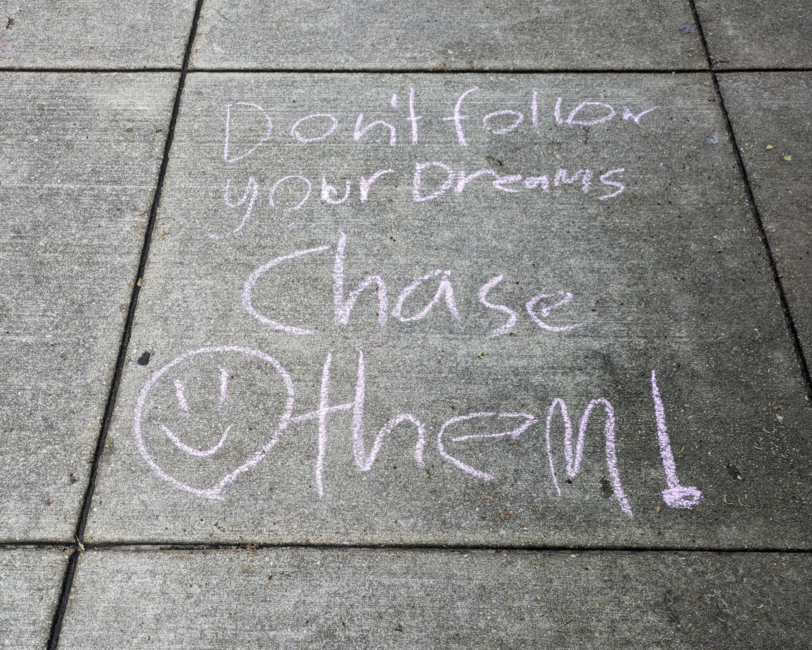 Pink chalk art of a smiley face with text "Don't follow your dreams, chase them!"